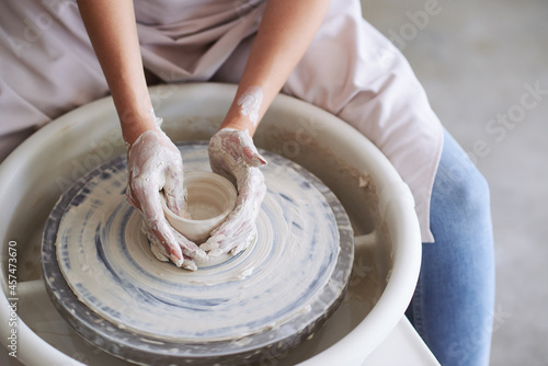 Hands of young woman working on pottery wheel in cozy workshop and making vase or mug