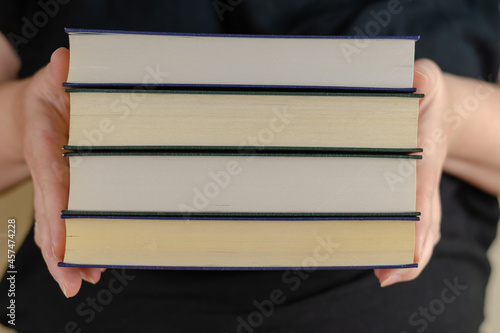 An adult Woman holding a stack of books. Woman's hands with hardcover textbooks. Close-up. Selective focus.