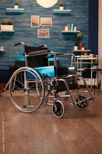 Empty living room in apartment with wheelchair on floor for disabled people. Nobody in indoors space decorated with modern furniture and walking support. Cozy interior with decorations