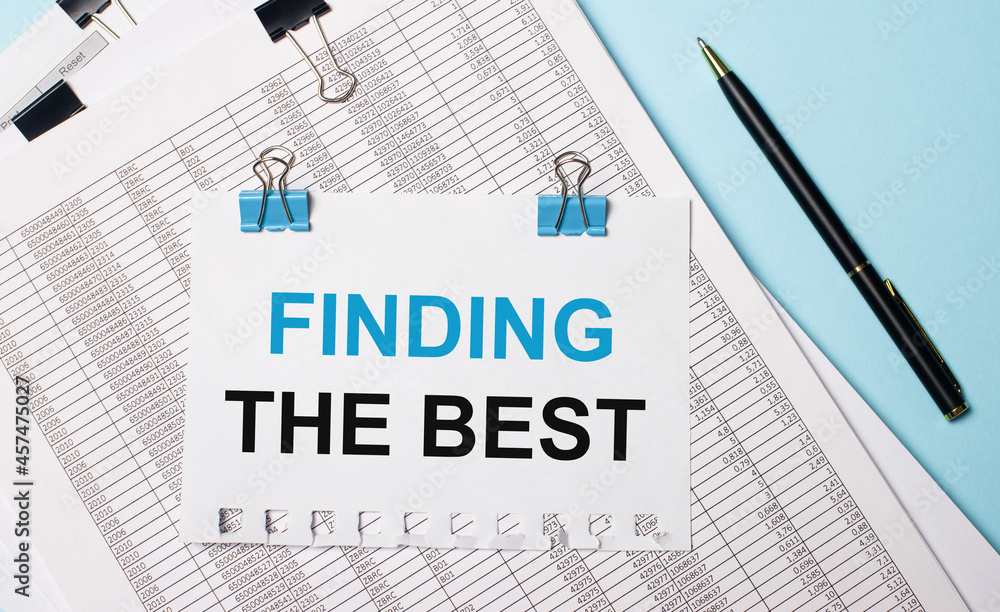 On a light blue background, documents, a pen and a sheet of paper on blue paper clips with the text FINDING THE BEST. Business concept. On a light blue background, documents, a pen and a sheet of paper on blue paper clips with the text FINDING THE BEST. Business concept.