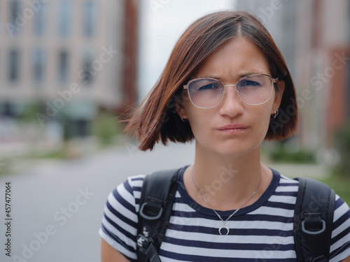 Close up face of beautiful Hispanic or Asian woman in glasses with brown hair outdoors. Confident stylish lady outdoor with copy space, emotional portrait of a tourist in the city