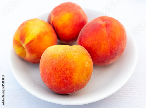 Ripe peaches in a white plate on the table.