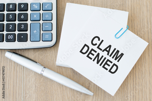 a white card with the inscription CLAIM DENIED on the table next to a calculator and a pen