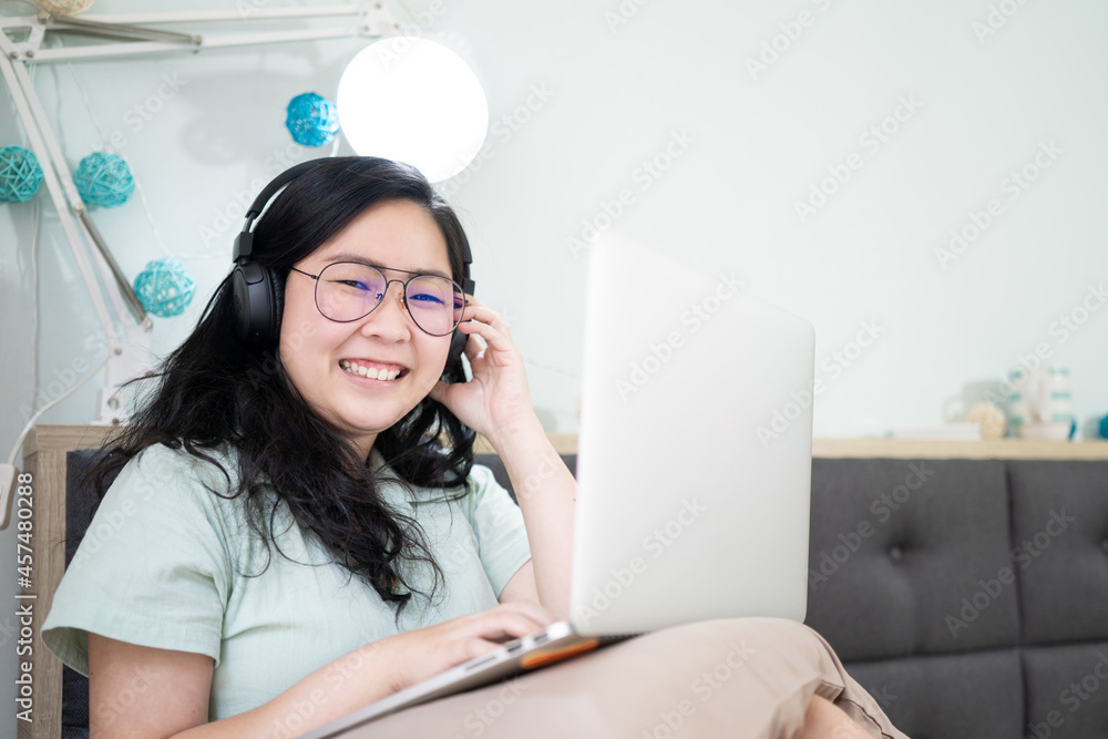 Glasses beautiful Asian woman is working on her laptop in the bedroom with a pastel green - brown color theme. Glasses beautiful Asian woman is working on her laptop in the bedroom with a pastel green - brown color theme.