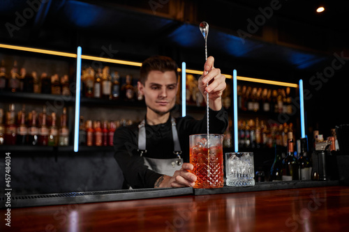 Barman stirring ice cubes in cocktail glass with spoon