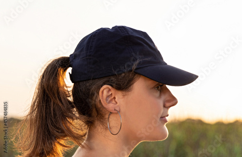 Teen girl in dark blue baseball cap at sunset