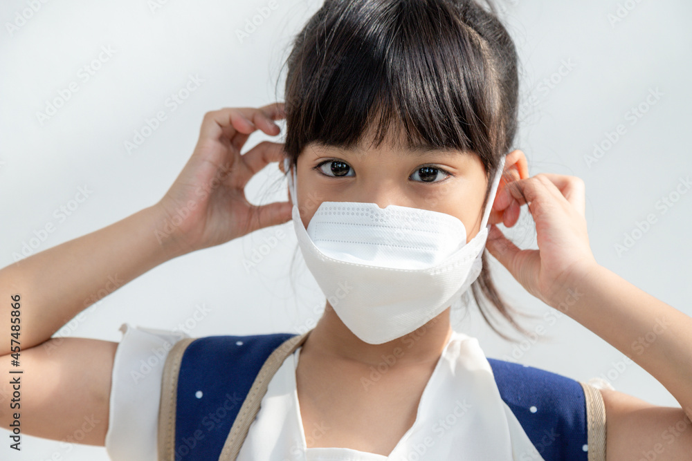 Asian girl in the white background wears a face mask that protects against the spread of coronavirus disease. Close-up of a little girl with a surgical mask on her face Asian girl in the white background wears a face mask that protects against the spread of coronavirus disease. Close-up of a little girl with a surgical mask on her face