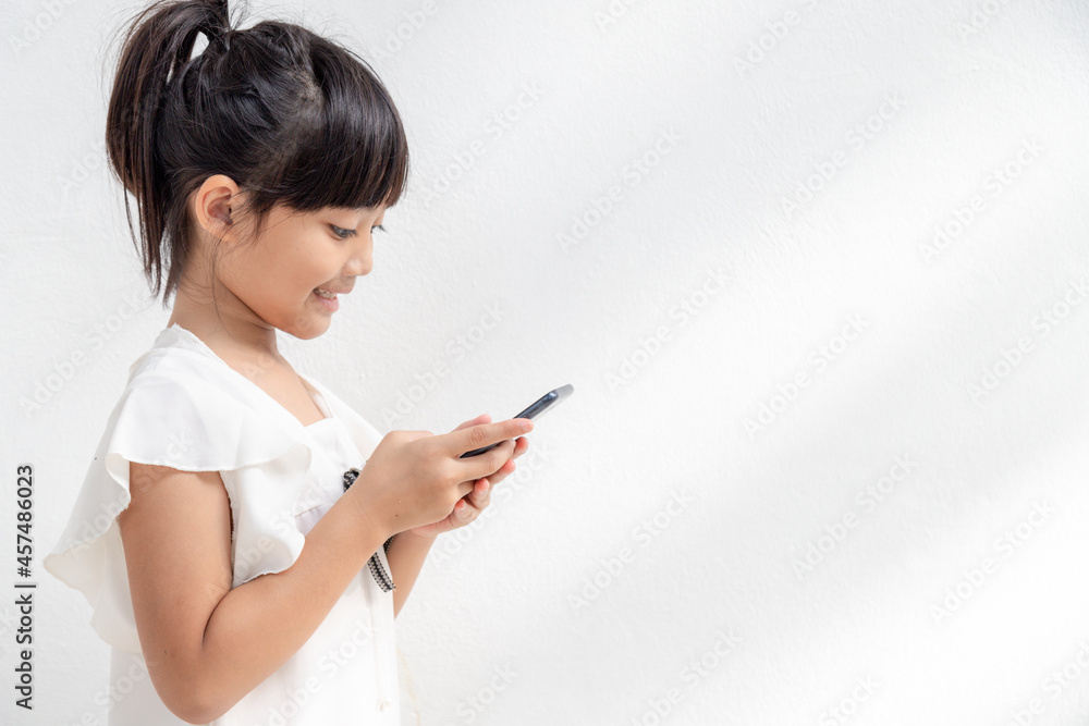 A little girl is concentrated on the phone, look at the smartphone, technology concept for children, profile view, isolated on white background, copy space A little girl is concentrated on the phone, look at the smartphone, technology concept for children, profile view, isolated on white background, copy space