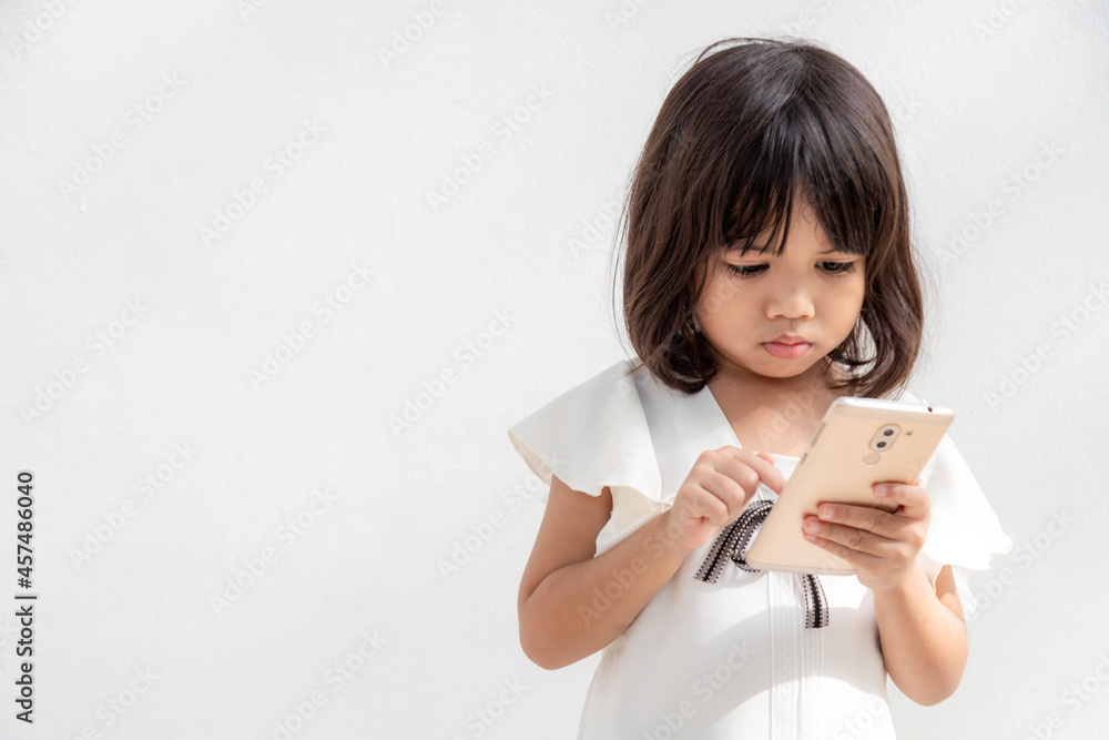 A little girl is concentrated on the phone, look at the smartphone, technology concept for children, profile view, isolated on white background, copy space A little girl is concentrated on the phone, look at the smartphone, technology concept for children, profile view, isolated on white background, copy space