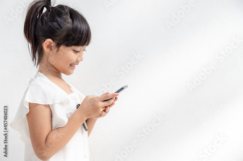 A little girl is concentrated on the phone, look at the smartphone, technology concept for children, profile view, isolated on white background, copy space