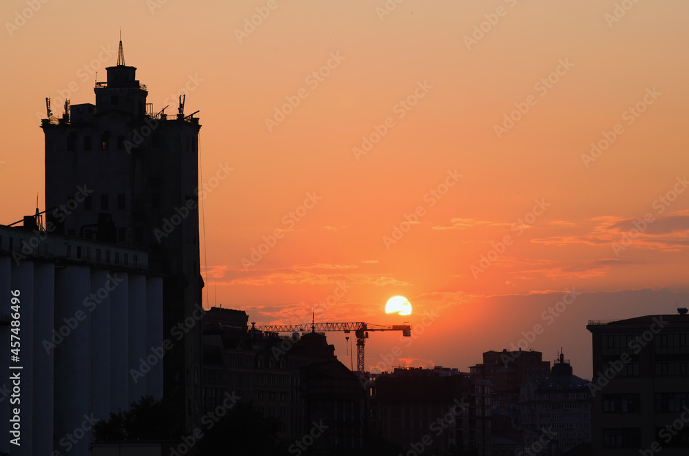 Amazing sunset cityscape in Kyiv. Black silhouette of the buildings against vibrant sky with bright sun disk