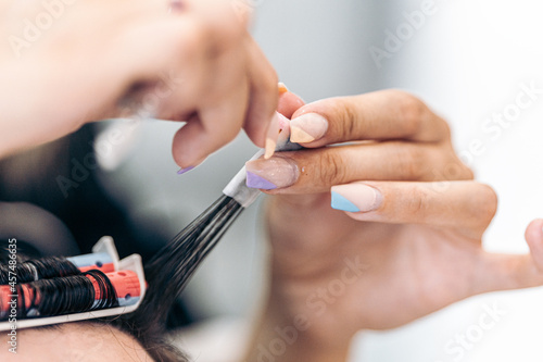 Focus on the painted nails of a hairdresser while curling the hair of a client