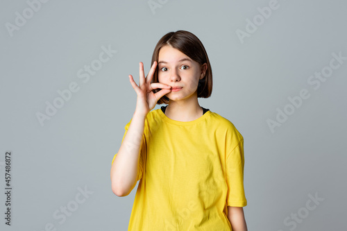 Fotografija Portrait of a pretty teen girl showing zip gesture as if shutting mouth on key, standing over light grey background