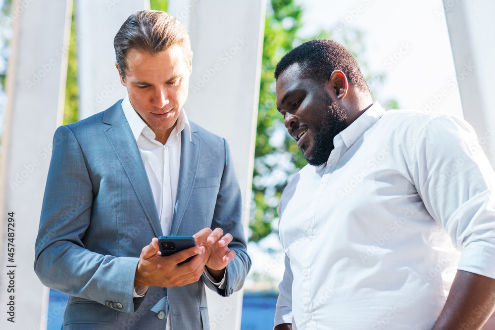 African-American businessman and his colleague in front of modern office building. Financial investors are talking outdoor. Banking and business concept. African-American businessman and his colleague in front of modern office building. Financial investors are talking outdoor. Banking and business concept.