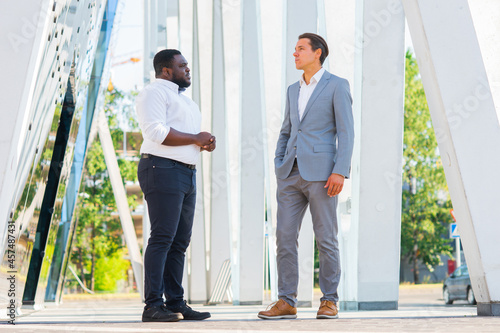 African-American businessman and his colleague in front of modern office building. Financial investors are talking outdoor. Banking and business concept.