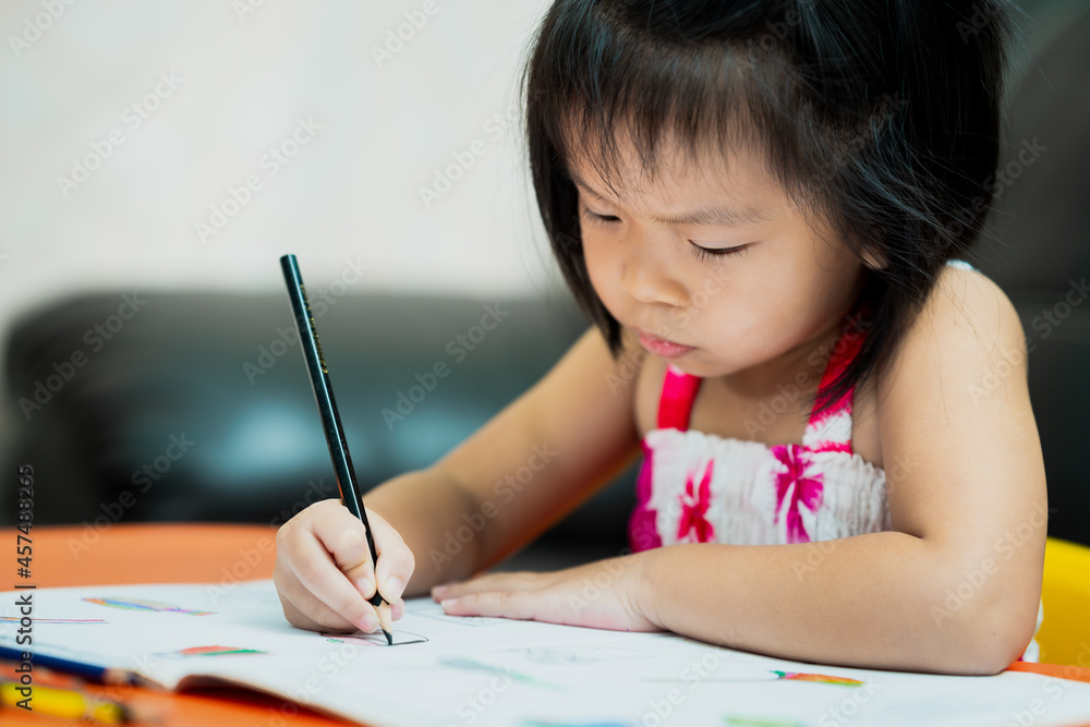 Asian cute kid holding black crayon coloring on book work. Serious girl with homework. Asian cute kid holding black crayon coloring on book work. Serious girl with homework.
