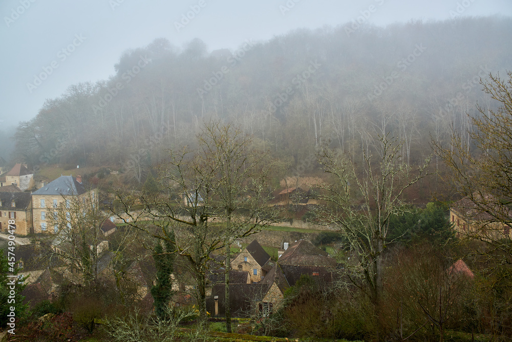 French town covered in mist next to a forest and mountains