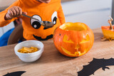 Close up of a little boy dressed as a halloween pumpkin emptying a halloween pumpkin in his kitchen at home. 