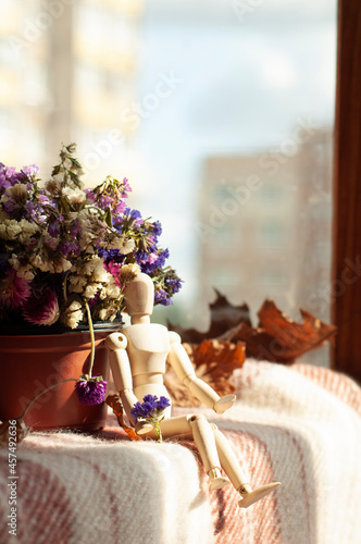 autumn mood. wooden man sits on a blanket near a vase of dried flowers