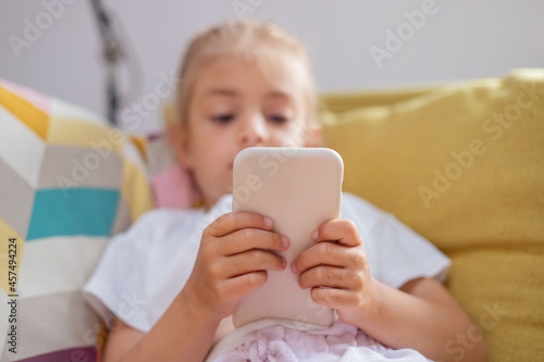 Close up of cute little 5s Caucasian girl child look at cellphone screen play online game on gadget.Kid using smart phone at living room.