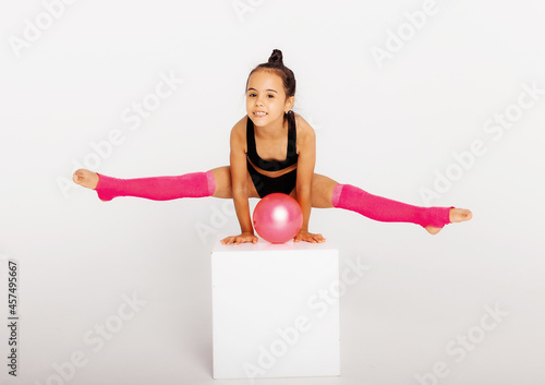Fotografie Little gymnast on a large white cube performs sports exercises