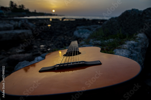 Canvas Print Closeup shot of a brown wooden guitar on the rocks at the seaside during late su