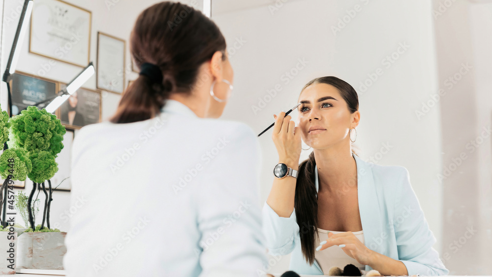 Woman paints her eyebrows looking into a mirror Woman paints her eyebrows looking into a mirror