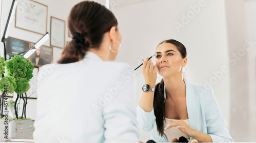 Woman paints her eyebrows looking into a mirror