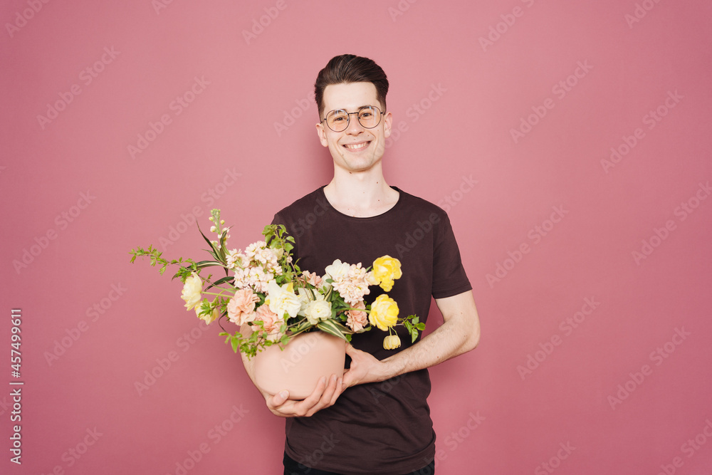 A young man is holding a beautiful bouquet of flowers in his hands on a pink background. The guy decided to make a surprise to his girlfriend. Mother's Day. Women's day. Flowers delivery. A young man is holding a beautiful bouquet of flowers in his hands on a pink background. The guy decided to make a surprise to his girlfriend. Mother's Day. Women's day. Flowers delivery.