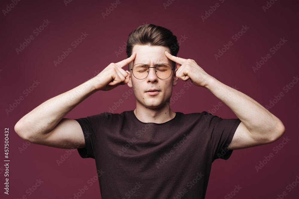 Fototapeta premium Young man in white t-shirt squeezing head with hands, suffering from headache. People, stress, tension and migraine concept