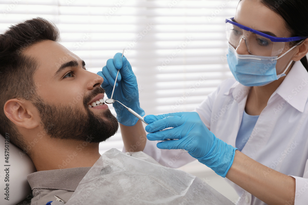 Dentist examining young man's teeth in modern clinic Dentist examining young man's teeth in modern clinic