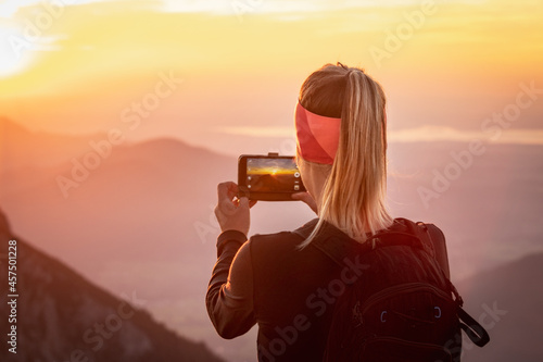 Hiking girl taking a picture of sunset  with her phone