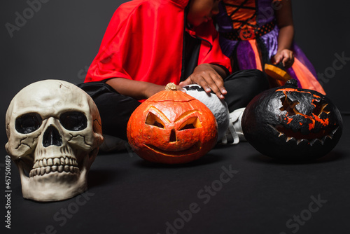 cropped view of african american siblings in halloween costumes holding carved pumpkins on black