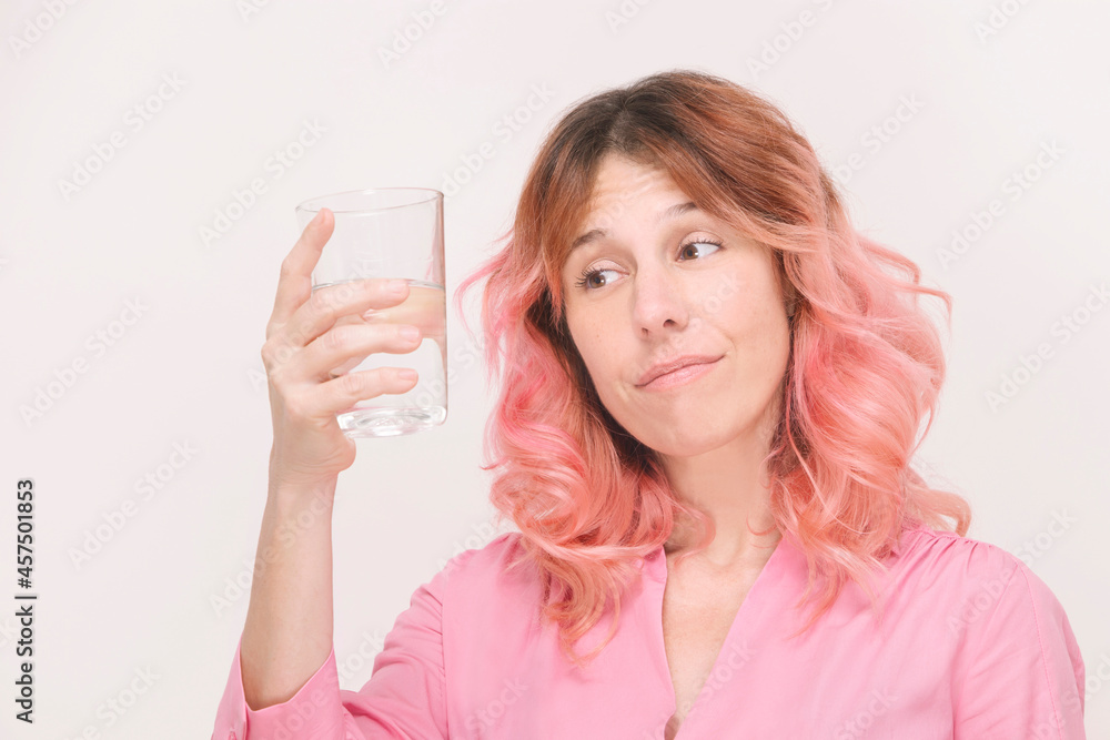 woman holding a glass of water and looking at it with a funny face on a white background woman holding a glass of water and looking at it with a funny face on a white background