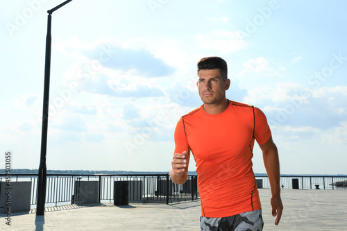 Handsome man in sportswear running outdoors on sunny day