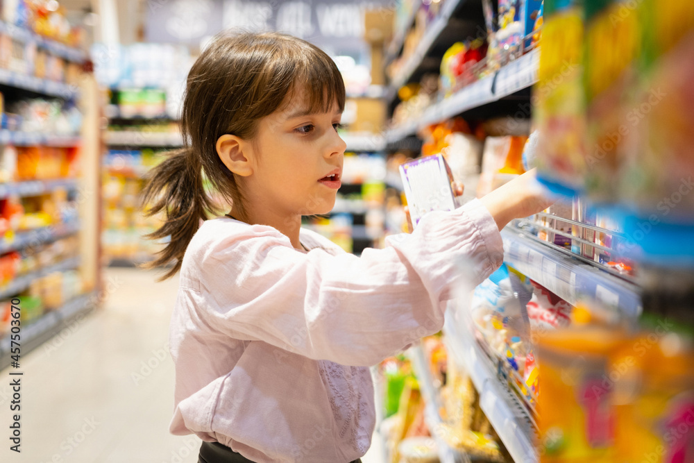 Close up photo of a girl with hairtail in the store choosing products in the department for children very attentively.