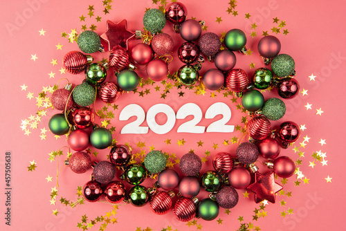 Wooden numbers 2022, green and red toy balls, and stars on a red paper background. Beautiful new year or christmas card top view