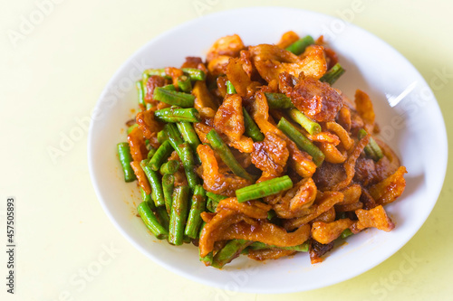 Stir fried crispy pork and yardlong bean with Thai spicy curry paste on white plate in Thai food style.