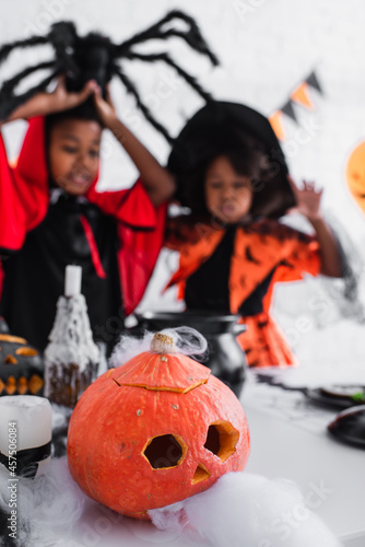 carved and creepy pumpkin near blurred african american children in costumes