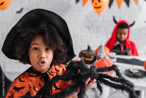 Foto spooky african american girl in witch costume holding toy spider near blurred br