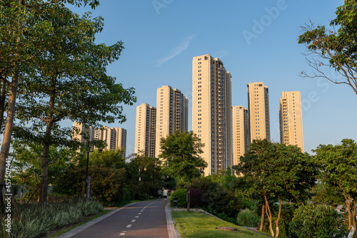 The road in the city park is surrounded by green trees. © chen