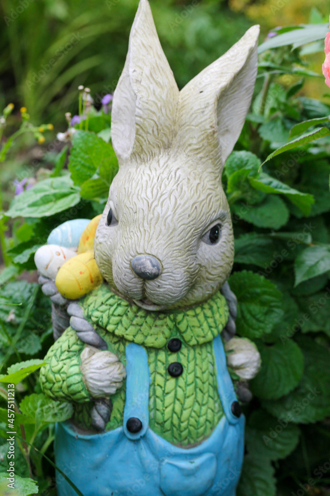 garden figure Easter bunny in blue jumpsuit with a backpack of colored eggs behind the back. garden figure Easter bunny in blue jumpsuit with a backpack of colored eggs behind the back.