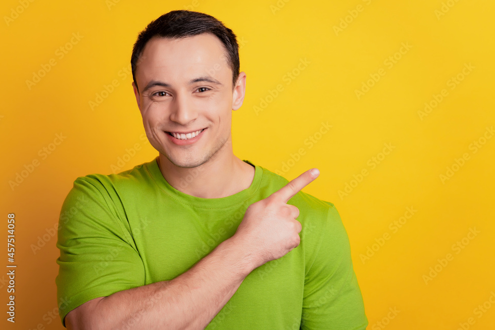 Portrait of positive guy indicate forefinger blank space show novelty on yellow background Portrait of positive guy indicate forefinger blank space show novelty on yellow background