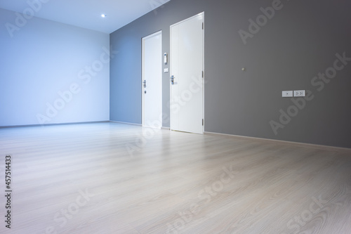 Closed wooden door inside empty room at perspective view. Entrance of room inside house building. Include wooden floor or laminate  white gray wall. New clean surface of wooden texture look modern.