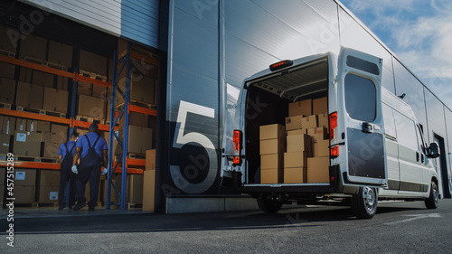 Outside of Logistics Distributions Warehouse: Two Workers Load Delivery Truck with Cardboard Boxes, Drive Off to Deliver Online Orders, Purchases, E-Commerce Goods. photo