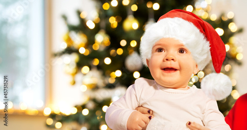 holidays and childhood concept - smiling baby girl in santa hat over christmas tree lights
