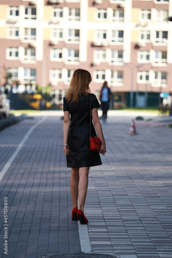 Slender woman in black dress walking in the street from the back