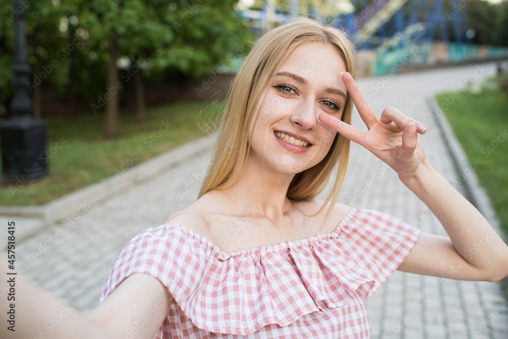 Young and attractive caucasian girl taking selfie on smartphone and showing peace gesture