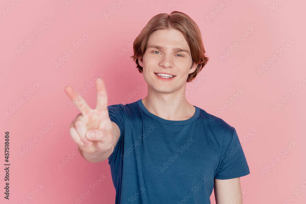 Photo of funny impressed young guy happy positive smile showing v-sign cool peace isolated pink color background Photo of funny impressed young guy happy positive smile showing v-sign cool peace isolated pink color background