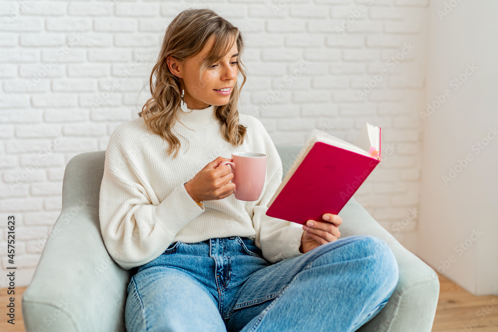 Lovely woman in warm soft sweater enjoing cup of tea and reading book in cozy winter morning. Lovely woman in warm soft sweater enjoing cup of tea and reading book in cozy winter morning.